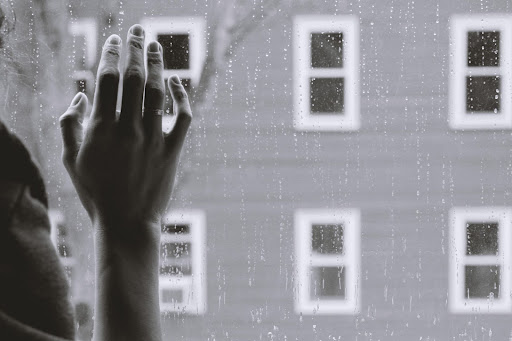 A womans hand on a window. She is looking at the rain outside.